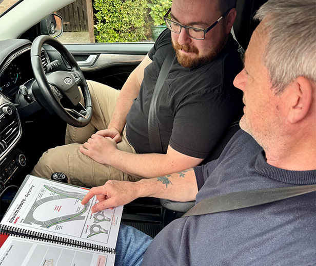 two men discussing driving concepts in a car with a layout guide showing circular designs and road instructions for a driving lesson